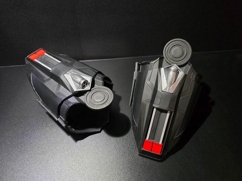 Puede incluir: Un par de lanzatelara&ntilde;as negros con detalles rojos y plateados. Los lanzatelara&ntilde;as tienen un bot&oacute;n circular en la parte superior y una peque&ntilde;a boquilla en el lateral.