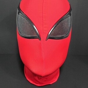 May include: A red superhero mask with black-rimmed eye openings. The mask is made of a smooth, stretchy material and covers the entire head and neck. The eye openings have a mesh texture.