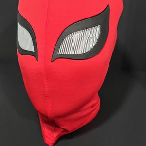 K&ouml;nnte beinhalten: Eine rote Stoffmaske mit schwarzen Augenkonturen und wei&szlig;en Augenabdeckungen aus Netzstoff. Die Maske ist so konzipiert, dass sie den gesamten Kopf und Hals bedeckt. Die Maske ist wahrscheinlich f&uuml;r Cosplay oder Kost&uuml;me gedacht.