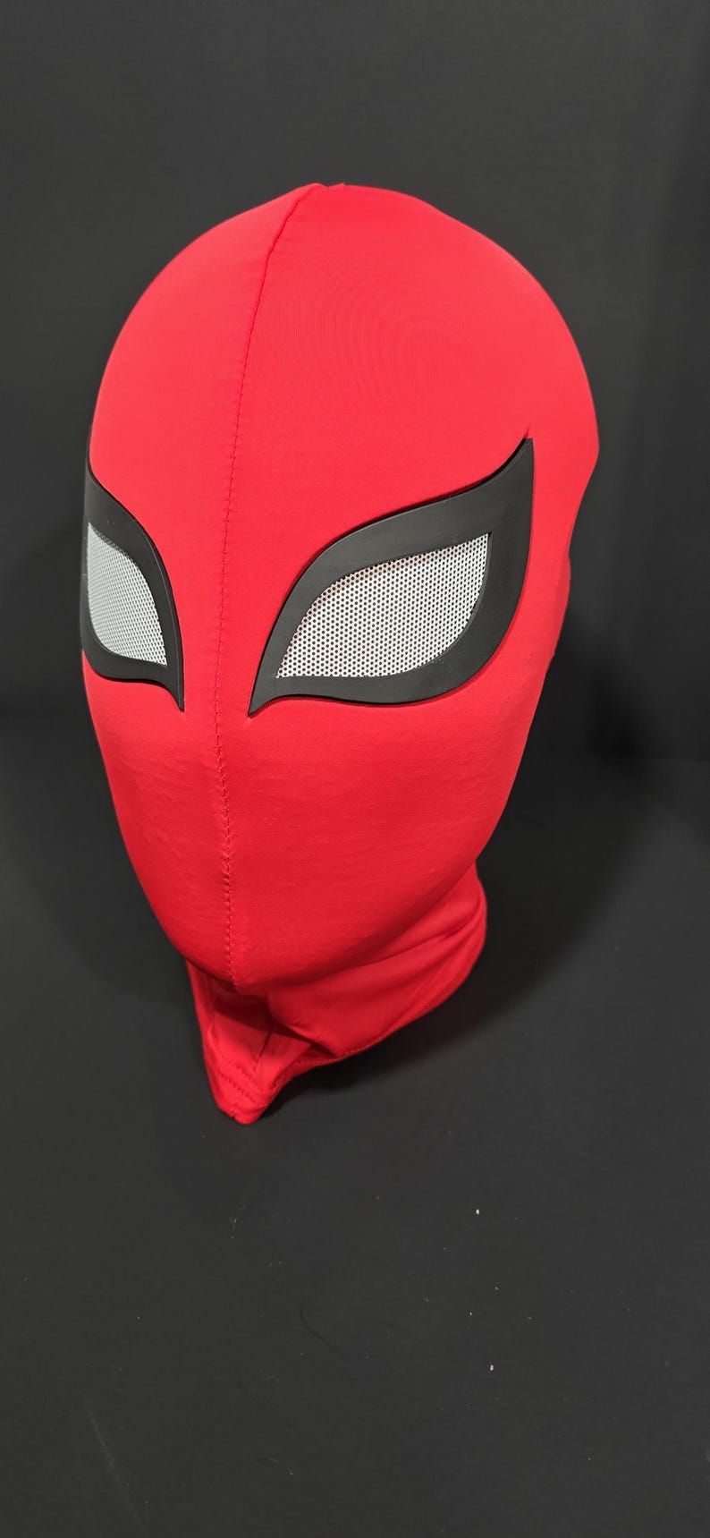 K&ouml;nnte beinhalten: Eine rote Stoffmaske mit schwarzen Augenkonturen und wei&szlig;en Augenabdeckungen aus Netzstoff. Die Maske ist so konzipiert, dass sie den gesamten Kopf und Hals bedeckt. Die Maske ist wahrscheinlich f&uuml;r Cosplay oder Kost&uuml;me gedacht.