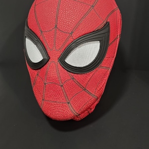 May include: A red Spider-Man mask with black webbing and eye frames. The eye lenses are white with a mesh pattern. The mask is a replica of the superhero's mask.
