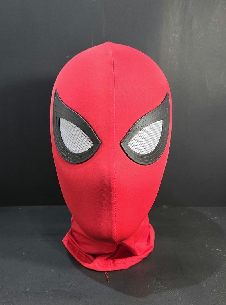 May include: A red Spiderman mask with black eye frames and mesh eye coverings. The mask is made of a soft fabric and covers the entire head and neck. The mask is a costume accessory.