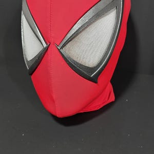 May include: A red Spider-Man mask with black trim around the eyes. The eye openings have a mesh material for visibility. The mask is made of a smooth, stretchy fabric and is designed to cover the entire head.