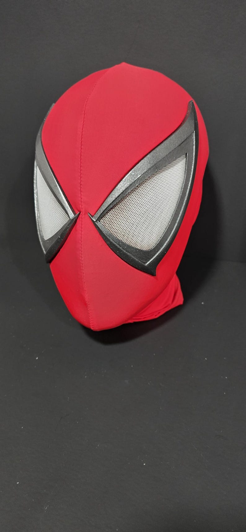 May include: A red Spider-Man mask with black trim around the eyes. The eye openings have a mesh material for visibility. The mask is made of a smooth, stretchy fabric and is designed to cover the entire head.