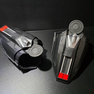 Puede incluir: Un par de lanzatelara&ntilde;as negros con detalles rojos y plateados. Los lanzatelara&ntilde;as tienen un bot&oacute;n circular en la parte superior y una peque&ntilde;a boquilla en el lateral.