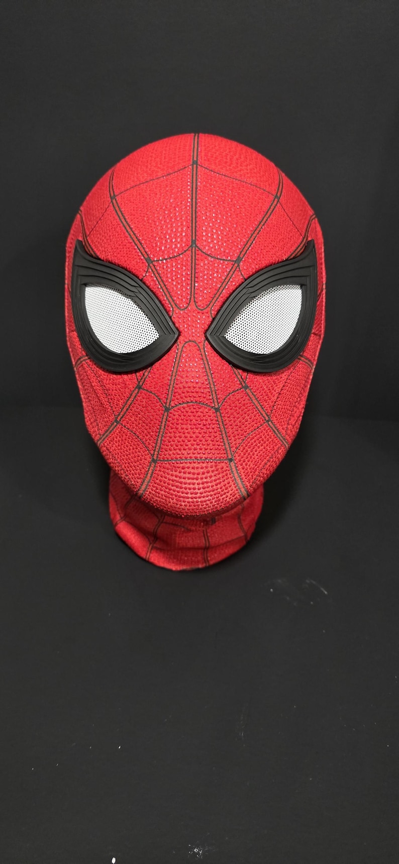 May include: A red Spider-Man mask with black accents and white mesh eye coverings. The mask features a textured surface and a web-like pattern. The mask is a cosplay item.