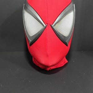 May include: A red Spider-Man mask with black and silver accents. The eye openings are framed in black and feature a mesh material. The mask is made of a soft, flexible fabric and is designed to cover the entire head.