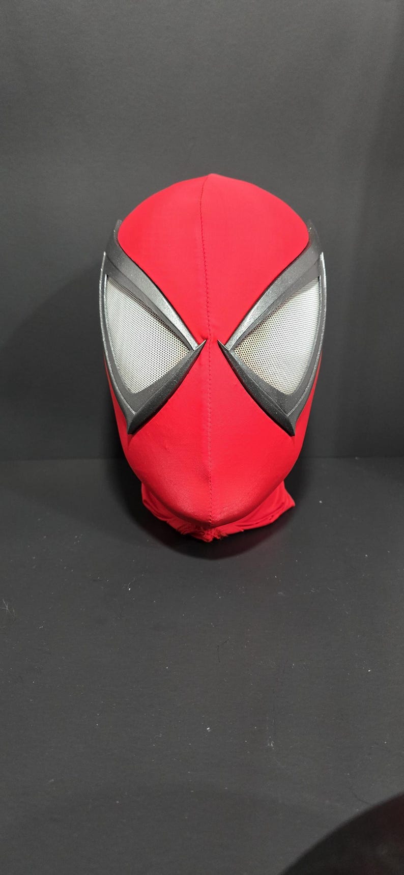 May include: A red Spider-Man mask with black and silver accents. The eye openings are framed in black and feature a mesh material. The mask is made of a soft, flexible fabric and is designed to cover the entire head.