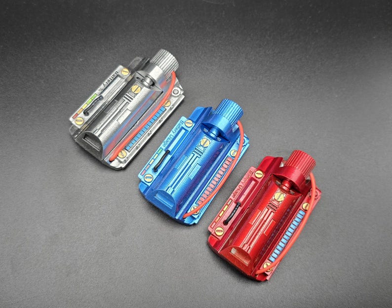 May include: Three rectangular metal battery pack props in silver, blue, and red. Each unit features a cylindrical knob, gold-colored screws, a red wire, and a printed label reading Battery Usage with a graphic indicator showing various colored bars.