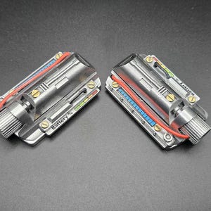 May include: Two metallic, rectangular electronic components featuring a silver finish, brass-colored screws, and a red wire. Each unit displays a battery level indicator with the text Battery % and a series of small blue and green square segments.