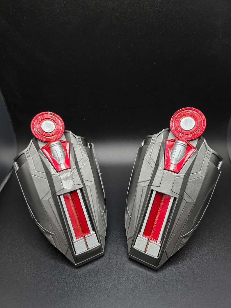 Puede incluir: Dos piezas de brazo de juguete de pl&aacute;stico negro y rojo con un c&iacute;rculo rojo en la parte superior. Las piezas de brazo tienen un dise&ntilde;o de rayas plateadas y rojas.