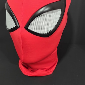 Peut inclure: Un masque en tissu rouge avec des contours d'yeux noirs et des revêtements oculaires en maille blanche. Le masque est conçu pour couvrir toute la tête et le cou. Le masque est probablement un article de costume ou de cosplay.