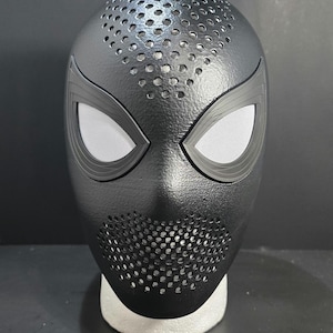 May include: Black Spider-Man mask with a textured surface and eye-shaped openings. The mask has a perforated design around the mouth and top of the head, and is likely a costume accessory.
