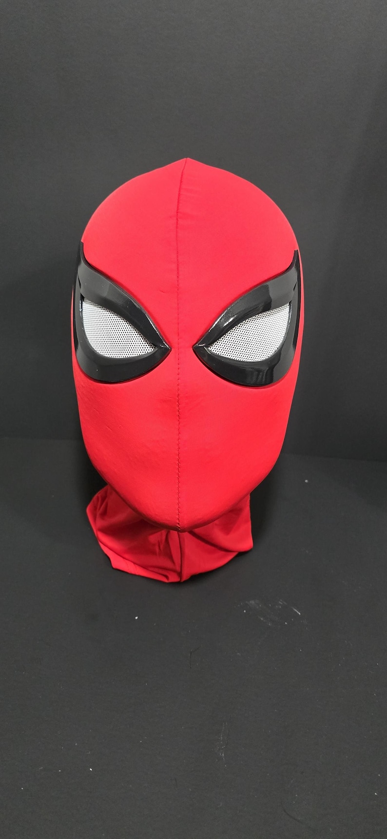May include: A red fabric mask with black eye surrounds and white mesh eye coverings. The mask is a full head covering, likely for cosplay or costume use.