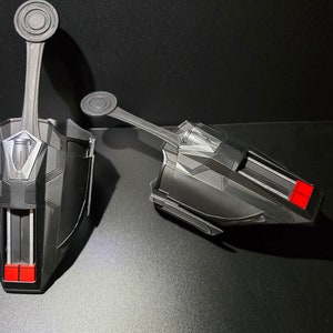 Puede incluir: Un par de lanzatelara&ntilde;as negros con detalles rojos. Los lanzatelara&ntilde;as tienen una superficie texturizada y un detalle plateado en la parte superior. Los lanzatelara&ntilde;as est&aacute;n dise&ntilde;ados para parecerse a los que usa Spider-Man.