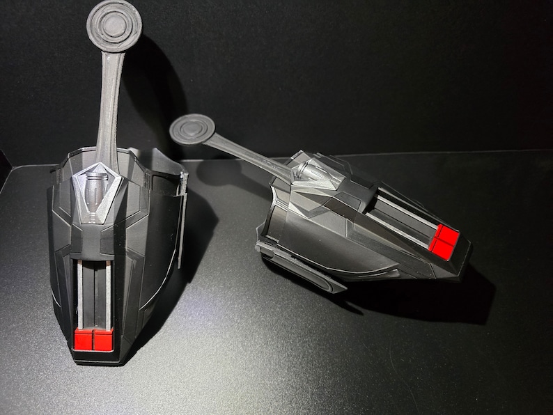 Puede incluir: Un par de lanzatelara&ntilde;as negros con detalles rojos. Los lanzatelara&ntilde;as tienen una superficie texturizada y un detalle plateado en la parte superior. Los lanzatelara&ntilde;as est&aacute;n dise&ntilde;ados para parecerse a los que usa Spider-Man.