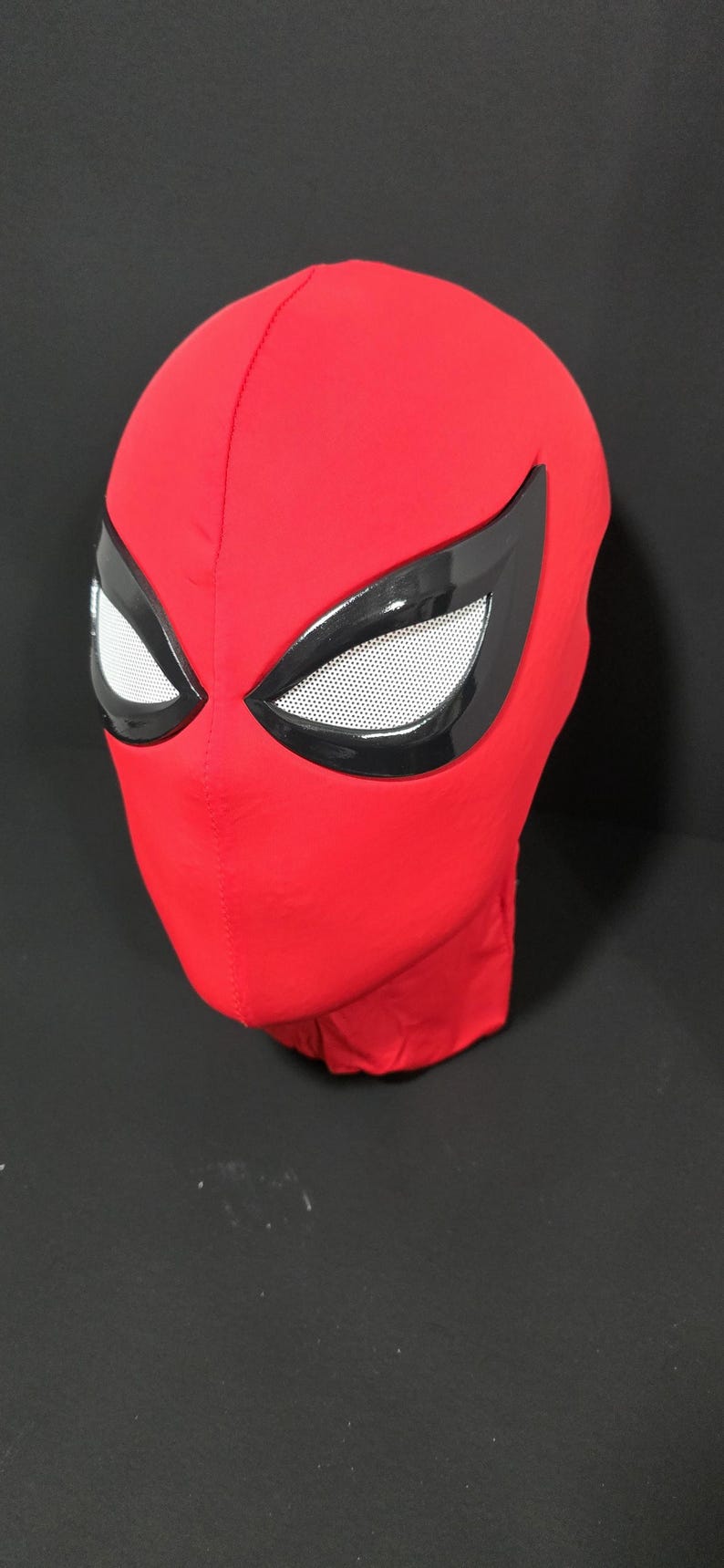May include: A red fabric mask with black eye coverings and white mesh eye inserts. The mask is designed to cover the entire head and face. The mask is likely for cosplay or costume use.