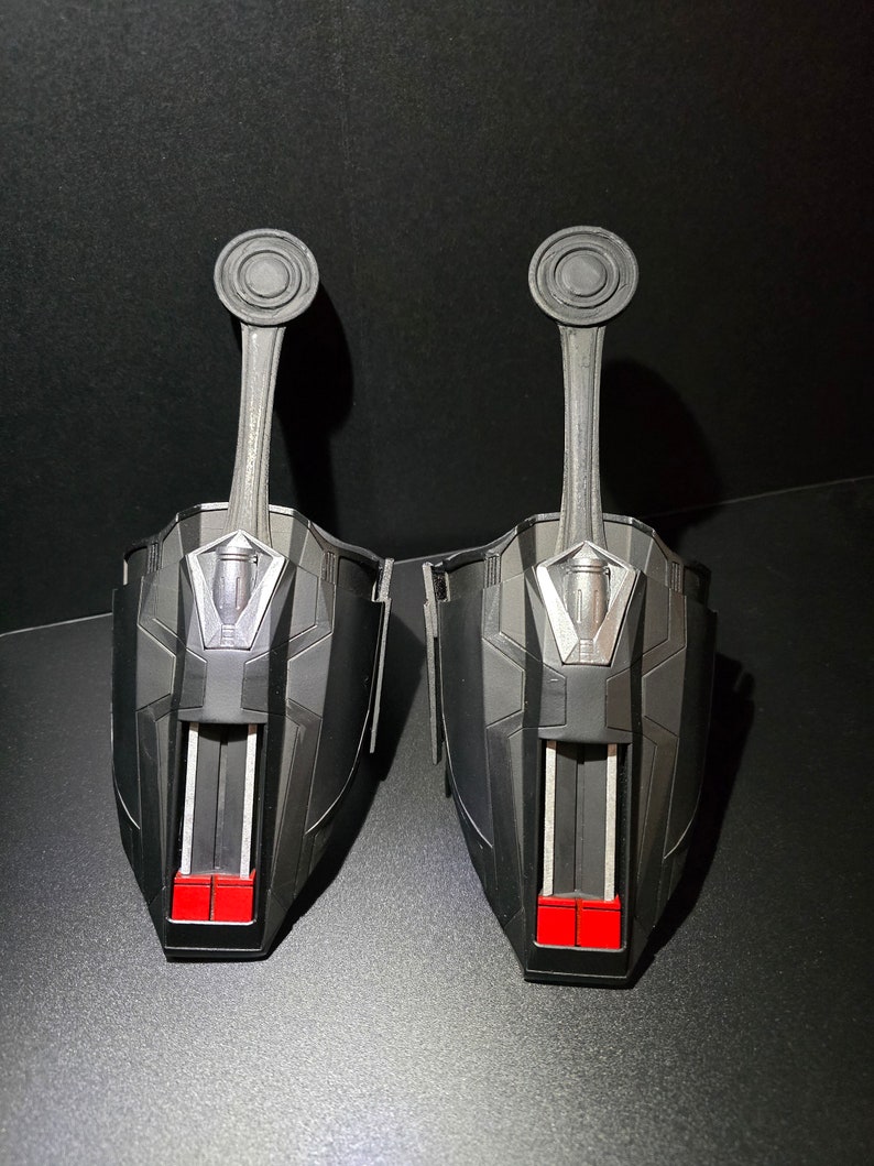 Puede incluir: Un par de lanzatelara&ntilde;as negros y plateados con detalles rojos. Los lanzatelara&ntilde;as tienen una palanca en la parte superior y un peque&ntilde;o compartimento en la parte inferior.