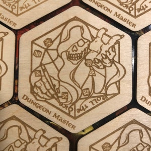 May include: A wooden hexagonal game token with a brown engraved design of a hooded skeleton figure holding a pen and a dice. The text "Dungeon Master" is engraved on the token.