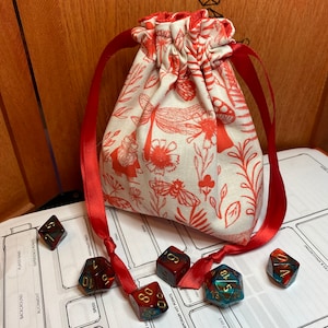Peut inclure: Un sac en tissu rouge et blanc avec un motif floral. Le sac est rempli de dés rouges, bleus et verts.