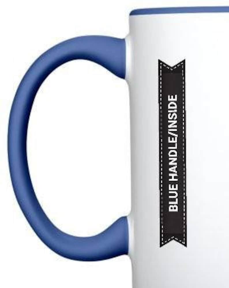 May include: White ceramic mug with a blue handle and rim. The mug has a black ribbon with the text "BLUE HANDLE/INSIDE" printed on it.