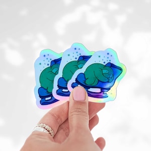 May include: Three holographic stickers featuring a cartoon sloth sleeping on a blue pillow. The sloth is green, and the pillow and base are blue. The stickers have a shimmering, iridescent effect and are shaped like a star.