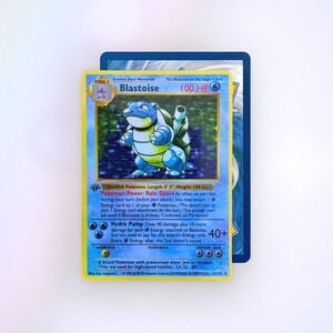 May include: A holographic Blastoise trading card featuring the character in a blue shell, 100 HP, and the Rain Dance Pokémon Power. The card text includes Shellfish Pokémon, Length: 5' 3", Weight: 189 lbs., Hydro Pump attack, and 1999 copyright.