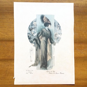 Op de afbeelding: Vintage mode-illustratie met een vrouw in een lange jurk en een gevederde hoed. Het kunstwerk is geplaatst in een cirkelvormig frame, met extra figuren en tekst zichtbaar. Het kleurenpalet omvat gedempte tinten grijs, bruin en beige.