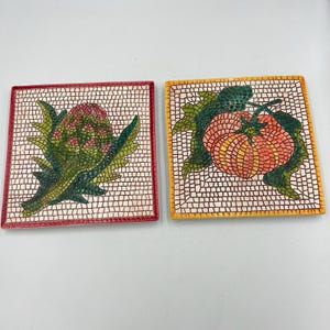 Puede incluir: Dos baldosas de mosaico cuadradas. Una baldosa presenta una alcachofa verde con detalles en rojo, la otra dos tomates naranjas con hojas verdes. Ambas baldosas tienen un fondo blanco con un patrón de mosaico.