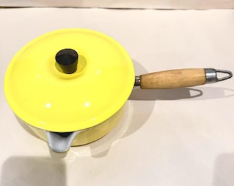 Cacerola Le Creuset n.º 18 amarilla con mango de madera, boquilla para verter y tapa de hierro fundido, fabricada en Francia en el siglo XXI.