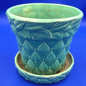 May include: A teal ceramic plant pot with a matching saucer, featuring a diamond-quilted pattern on the body and a sculpted leaf border around the rim. The glaze has a visible crackle finish throughout the interior and exterior surfaces.