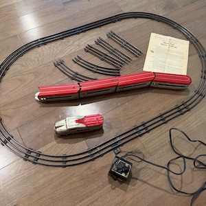 May include: A vintage electric train set featuring a red and silver diesel locomotive, three matching passenger cars, a black oval track, a power controller with a cord, and an instruction sheet titled Diesel Type Electric Train Set.