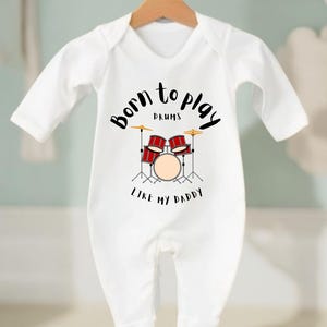 May include: White baby grow with a black graphic that says "Born to Play Drums Like My Daddy" with a cartoon drum set.