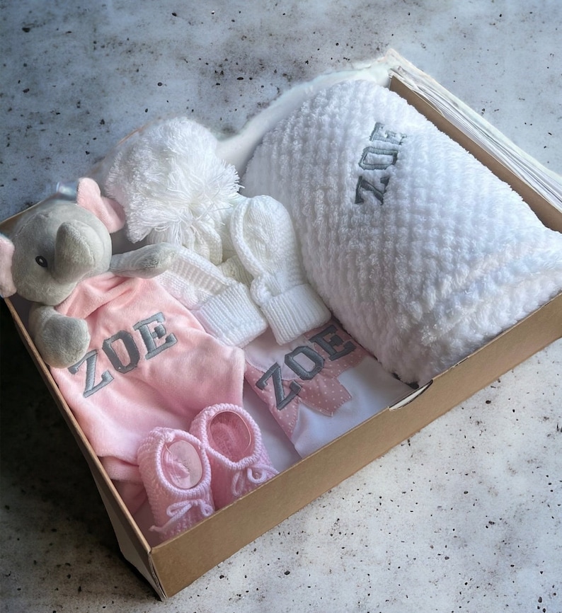 Pink Baby Gift Set featuring a personalized baby blanket, adorable baby elephant comforter, personalized baby bib, cozy baby knitted hat, soft baby mittens, and cute baby knitted booties.