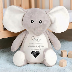 May include: A gray plush elephant with large white ears and a white belly. The word "Daddy" is written on the belly, along with a poem and a sonogram image. The elephant is sitting on a blue surface.