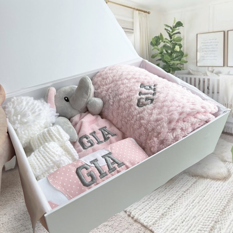 Pink Baby Gift Set featuring a personalized baby blanket, adorable baby elephant comforter, personalized baby bib, cozy baby knitted hat, soft baby mittens, and cute baby knitted booties.