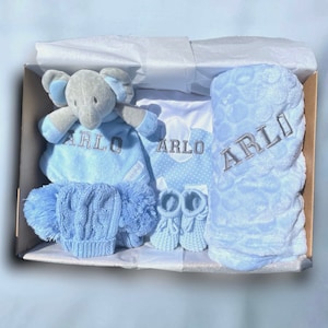 personalised newborn baby gift in blue, includes blue elephant comforter, soft blue blanket, blue/white elephant bib all personalised, blue knitted wool hat, mittens and booties. Dark grey personalised embroidery. Inside gift box.