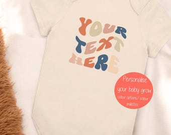 May include: A beige baby onesie with the text "YOUR TEXT HERE" in colorful, wavy letters. The text is in a retro style font. The onesie is on a white background.