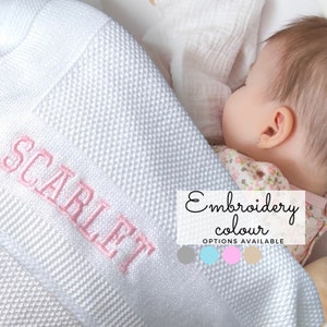 May include: White knitted baby blanket with the name "SCARLET" embroidered in pink. The blanket is shown with a baby sleeping on it. The text "Embroidery colour OPTIONS AVAILABLE" is shown below the blanket with four color swatches: gray, blue, pink, and beige.