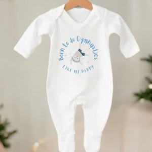 Puede incluir: Mono blanco de manga larga para bebé con una ilustración azul y blanca de un bebé haciendo gimnasia. El texto dice "Nacido para hacer gimnasia como mi papá."