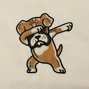 Könnte beinhalten: Weißes Baumwoll-Geschirrtuch mit einem gestickten Bild eines braunen und weißen Hundes, der den Dab macht.