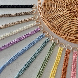 Puede incluir: Un conjunto de 10 llaveros de macramé con anillos de madera. Los llaveros son de varios colores, incluyendo negro, beige, blanco, rosa claro, azul claro, verde claro, amarillo, naranja, marrón y rosa.