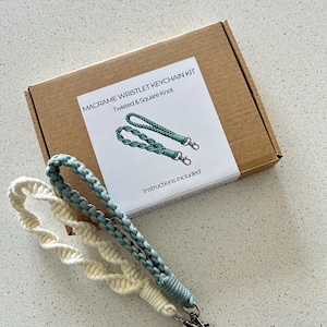 May include: A macrame wristlet keychain kit with twisted and square knot designs. The kit includes a box with instructions and two finished keychains, one cream-colored and one teal, each with a silver-colored clasp.