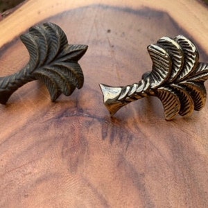 May include: Two palm tree shaped metal drawer pulls. One is a dark bronze color and the other is a shiny gold color.