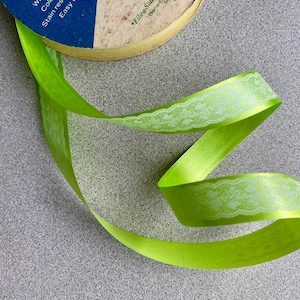 May include: A green satin ribbon with a white lace pattern. The ribbon is curled and twisted, showing off the delicate lace design.