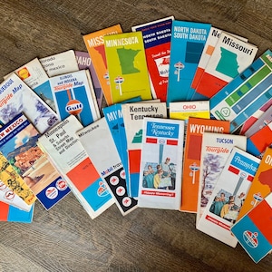 May include: A collection of vintage travel maps and tour guides, featuring various states and cities. The maps have colorful designs and logos, including those of Mobil and Gulf. The maps are from the 1970s.