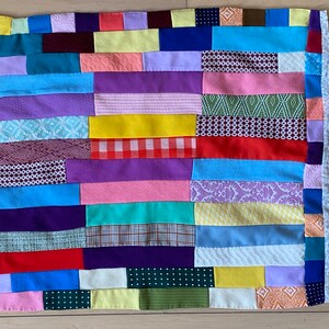 May include: A colorful patchwork quilt with a variety of fabrics and patterns, including floral, geometric, and plaid. The quilt is made up of horizontal strips of fabric sewn together.