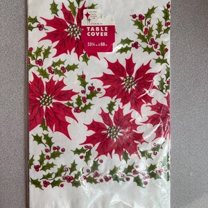 May include: A white table cover with a festive poinsettia and holly design. The red poinsettias are surrounded by green holly leaves and red berries. The table cover measures 53.5 x 88 inches.