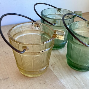 May include: Three glass buckets with metal handles. The buckets are in shades of green and yellow. The buckets are textured to look like wood.