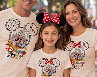Op de afbeelding: Drie crèmekleurige t-shirts met een afbeelding van een Mickey Mouse-oorsilhouet gevuld met een kasteel en Disney-figuren, vuurwerk, de tekst Disney 2021, individuele labels voor Dad, Mom en Lizy, en een rode haarband met stippen.